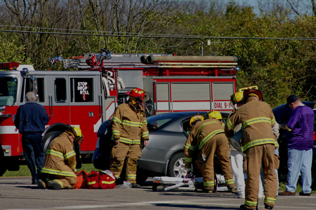 auto accident scene with firetruck and firemen using a stretcher to remove injured person from wrecked car